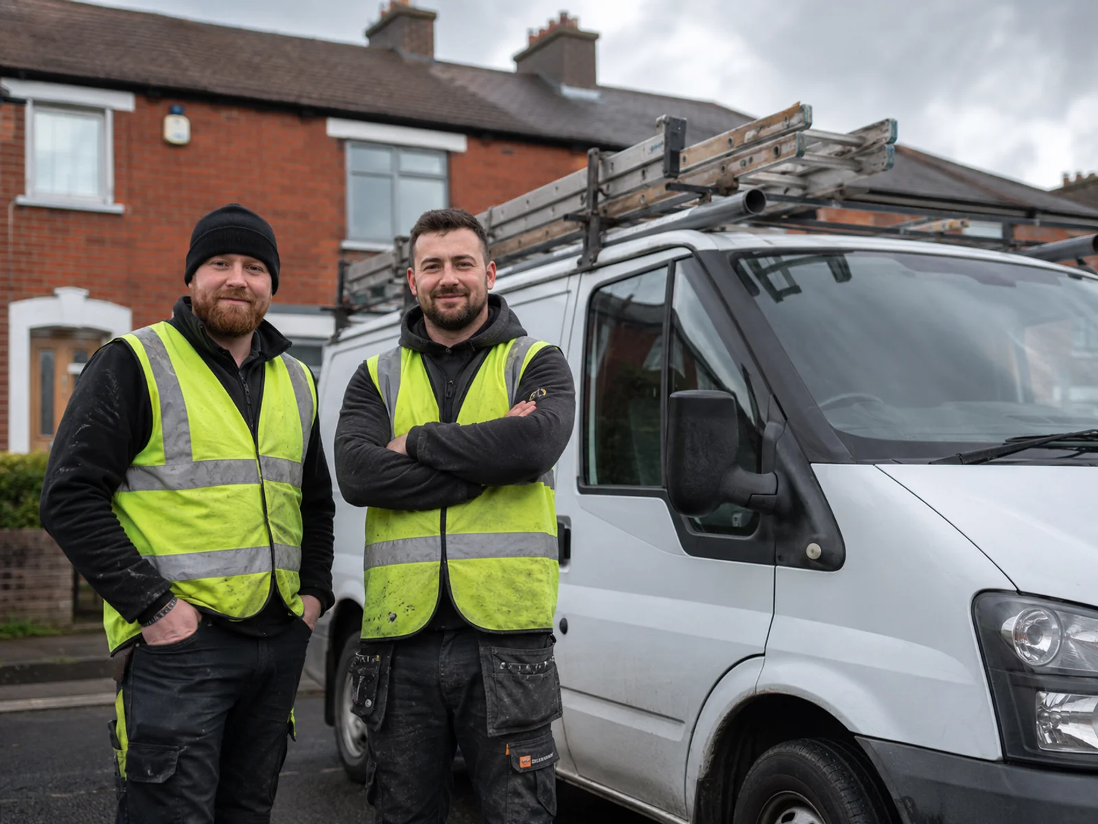 Two tradespeople beside a white transit van on a Dublin redbrick street in Artane